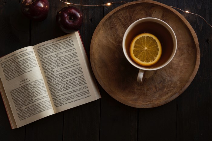 Open book, tea with orange slice, and apples on a wooden tray