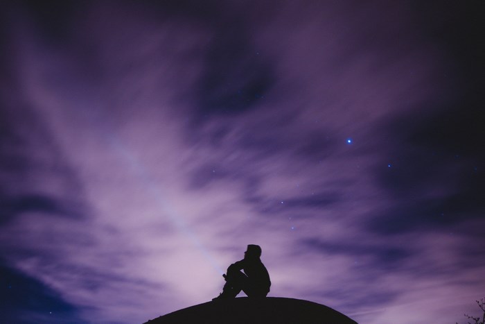 Silhouette of a person sitting under a starry, cloudy night sky