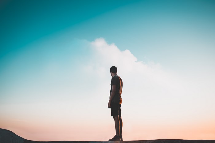 Man standing on edge against colorful sky