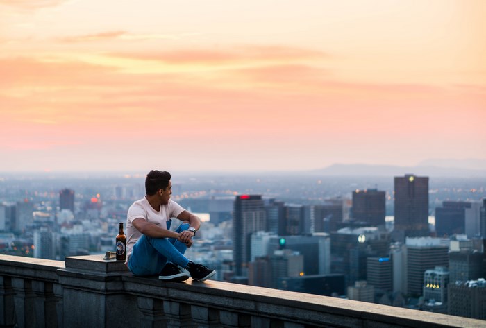 Man sitting on a ledge with a beer overlooking Montreal at sunset