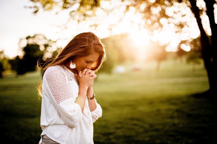 Woman praying in a park at sunset