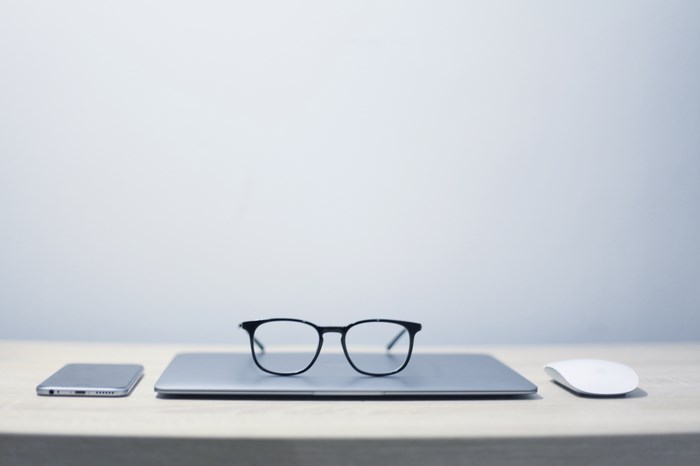 Minimalist desk setup with laptop, glasses, phone, and mouse