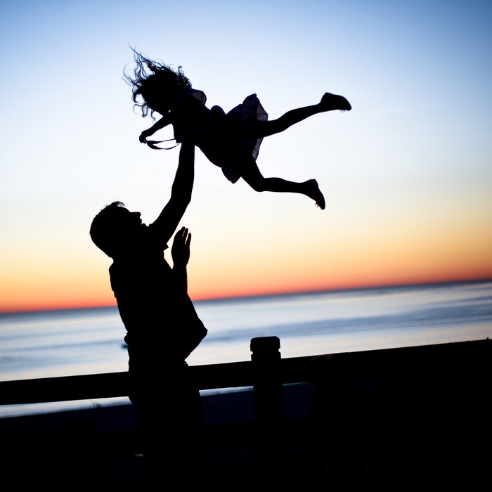 Father throws daughter in the air at sunset