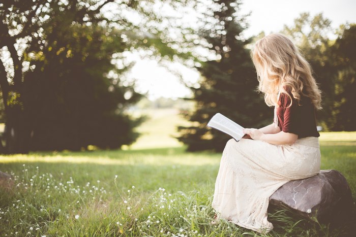 Woman reading a book on a rock in a park