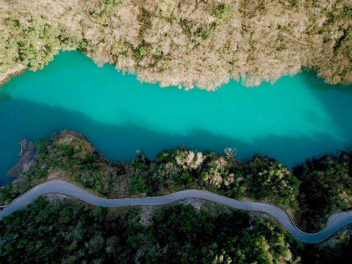 Aerial view of a winding road next to a turquoise lake and forest