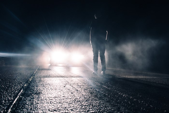 Man standing on wet road at night with car headlights