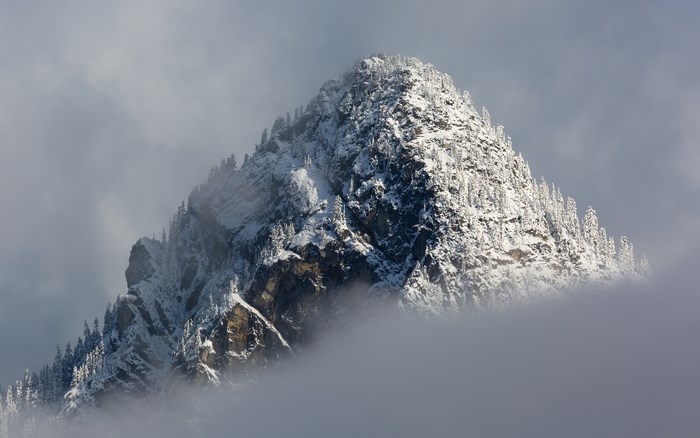 Snow-covered mountain peak emerging from clouds
