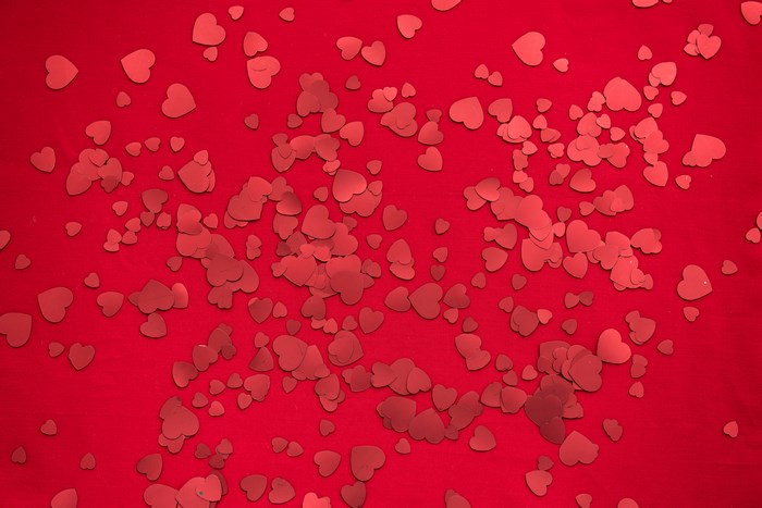 Red heart confetti scattered on a red background