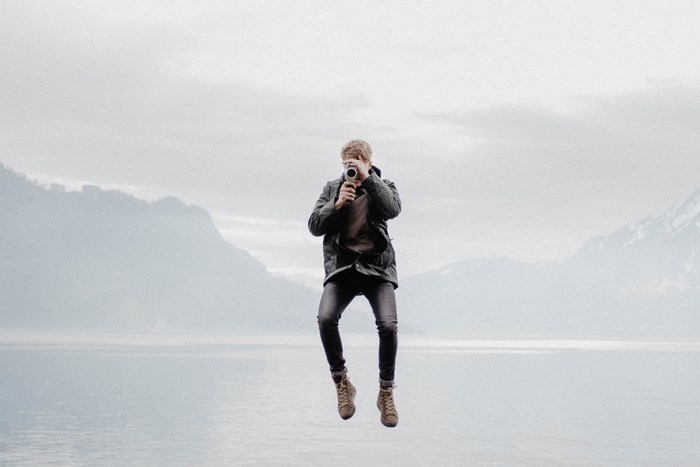 Man jumping while holding a camera over a lake