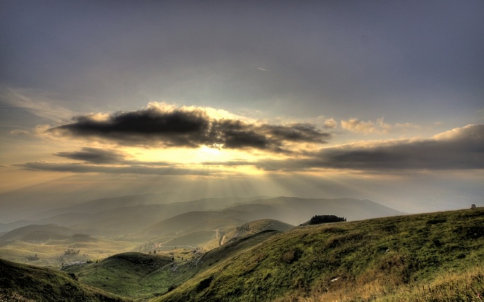Sunbeams through clouds over rolling hills