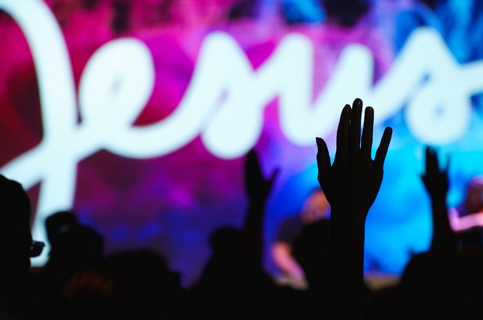 People raising hands in front of Jesus sign