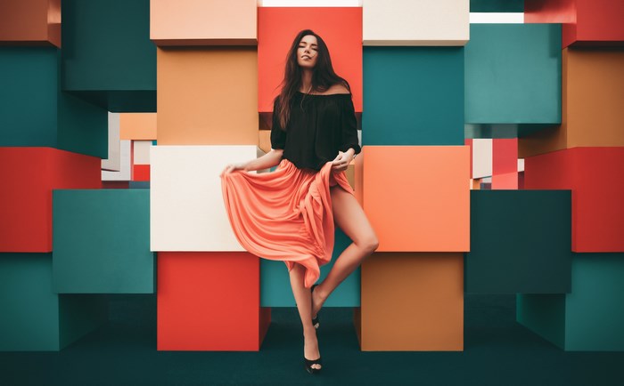 Woman in black top and orange skirt posing against colorful blocks