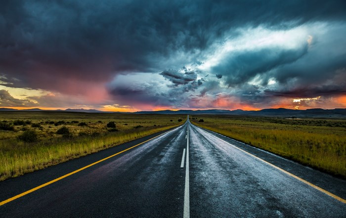 Road through a plain at sunset with dramatic clouds
