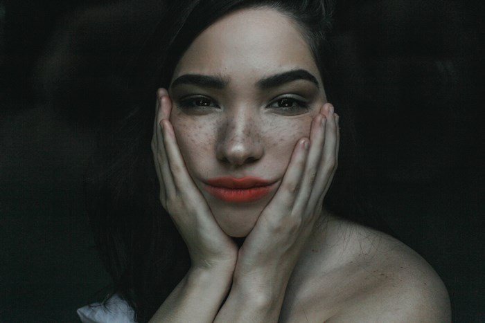 Woman with freckles and red lipstick holding her face