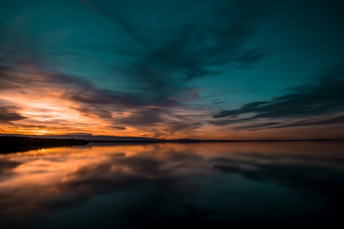 Moody sunset over calm water with orange and teal clouds