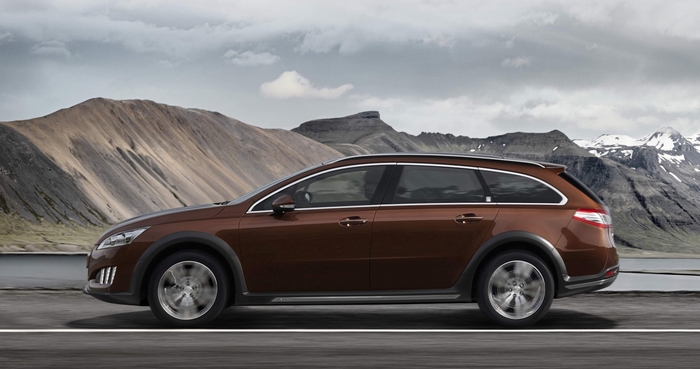 Brown station wagon driving on a road with mountains