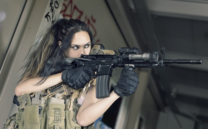 Woman in tactical gear aiming assault rifle