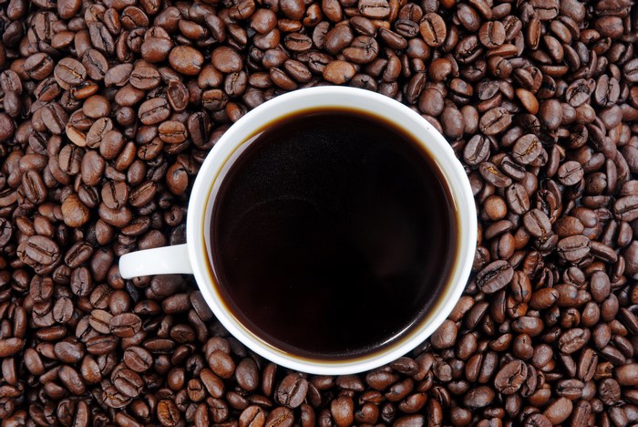 Coffee cup filled with dark coffee surrounded by coffee beans
