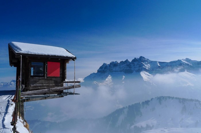 Wooden cabin on a cliff edge with snowy mountains