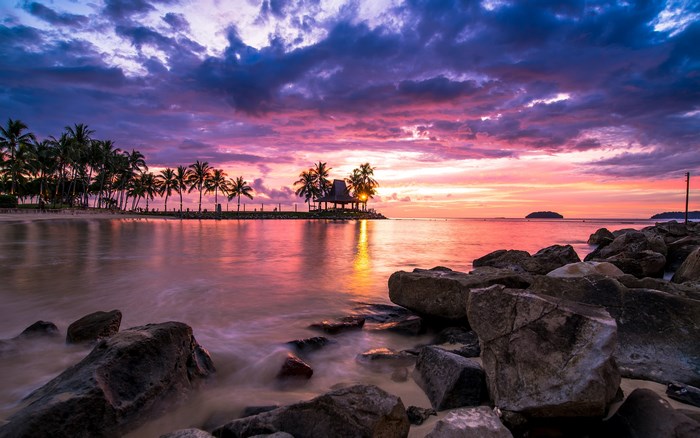 Tropical beach sunset with palm trees and rocks