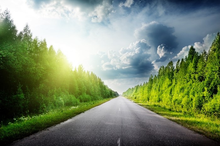 Road through a forest with sun and clouds