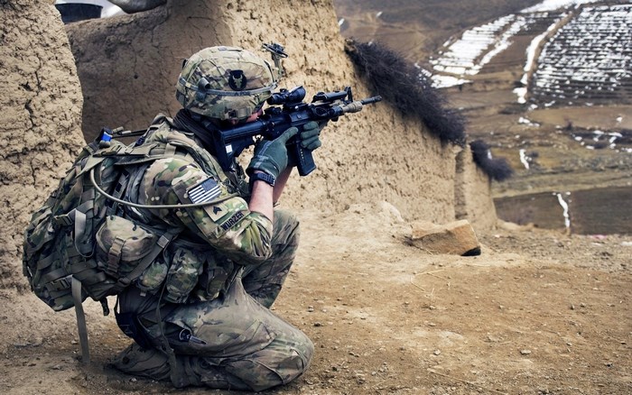 Soldier in camouflage gear aiming a rifle