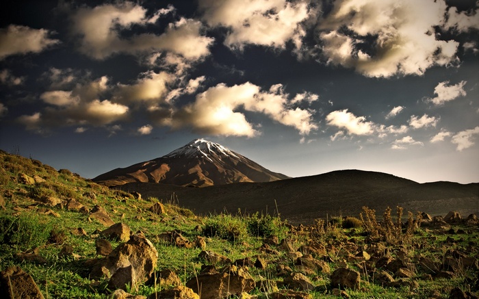 Snow-capped mountain under cloudy sky with rocky foreground