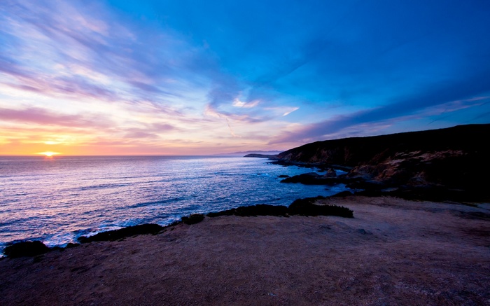 Sunset over the ocean with rocky coastline