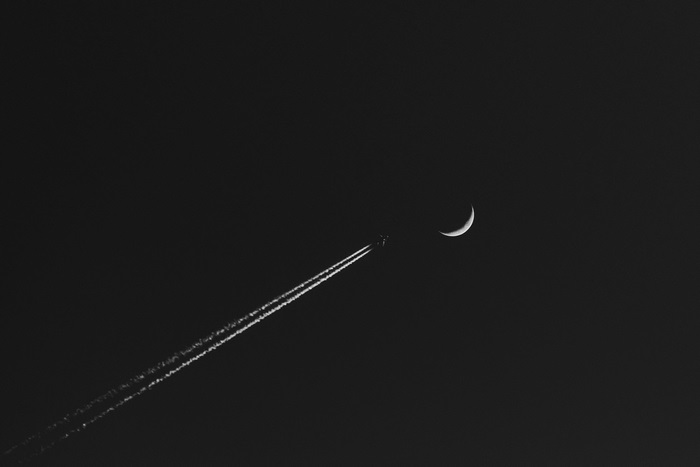 Airplane leaving contrail near crescent moon