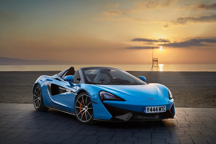 Blue McLaren 570S Spider convertible car on beach at sunset