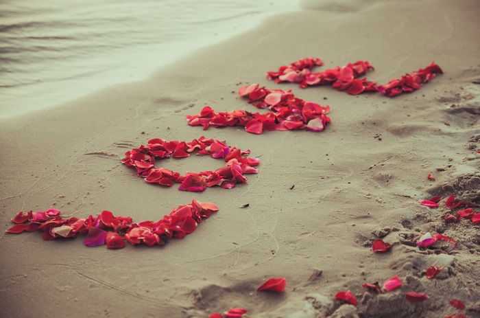 Love spelled with rose petals on a beach