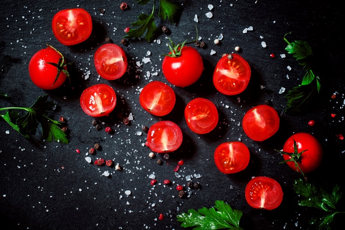 Tomatoes with salt and pepper on a dark surface