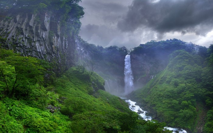 Waterfall in a lush green forest under cloudy skies in Japan