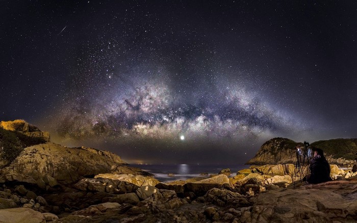 Milky Way over rocky coast with photographer