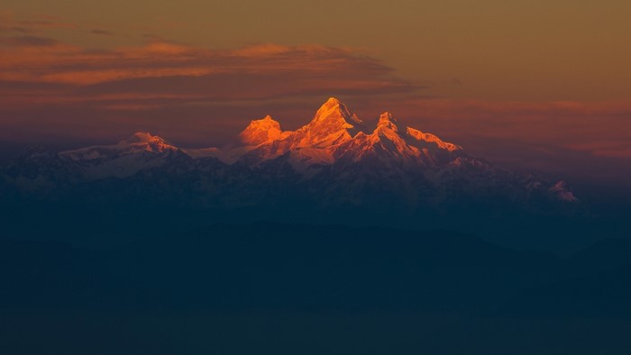 Snowy Himalayan peaks at sunset with orange clouds