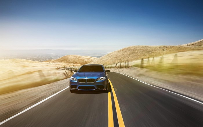 Blue BMW M5 driving on a scenic road