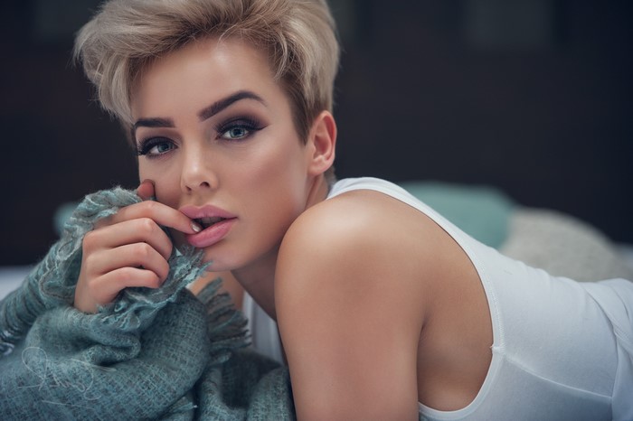 Woman with short blonde hair and finger in mouth