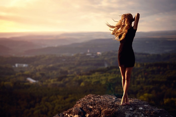 Woman in black dress on a rock overlooking a landscape
