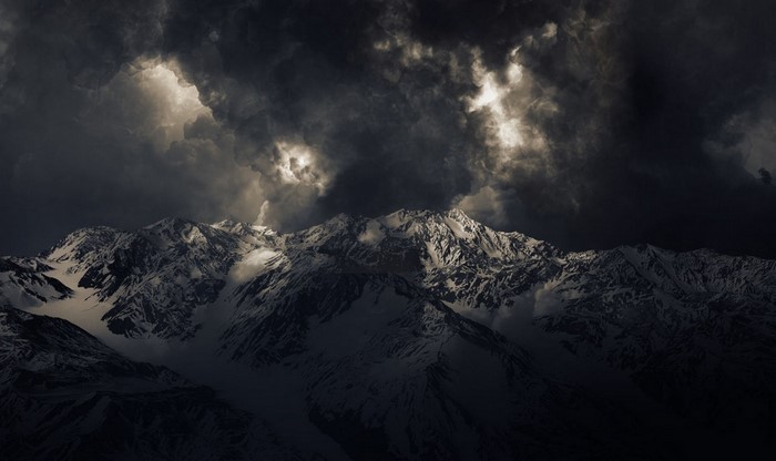 Snowy mountains under dark storm clouds with sunlight breaking through