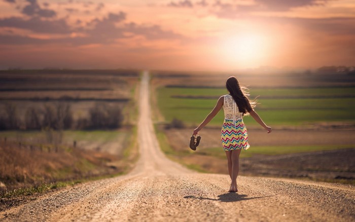 Woman walking barefoot on a dirt road at sunset