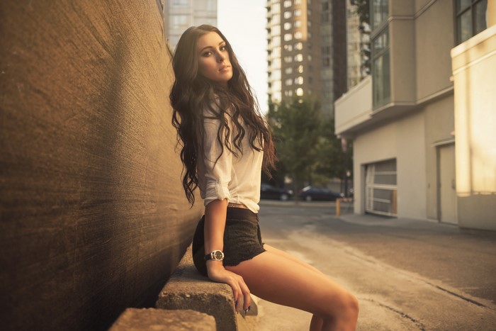 Woman in white shirt and black shorts sitting by wall
