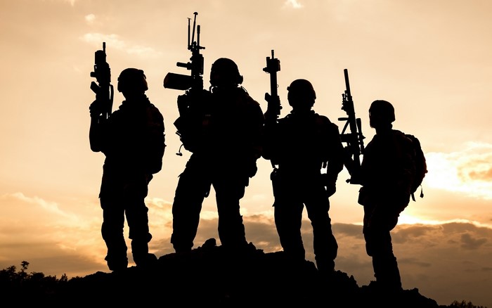 Silhouette of soldiers with assault rifles at sunset
