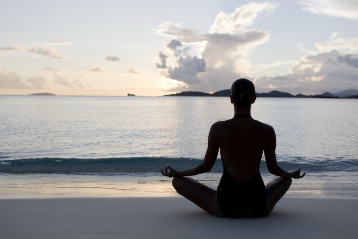 Woman meditating on a beach at sunset