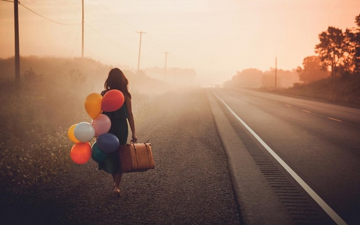 Woman with balloons and suitcase on a foggy road