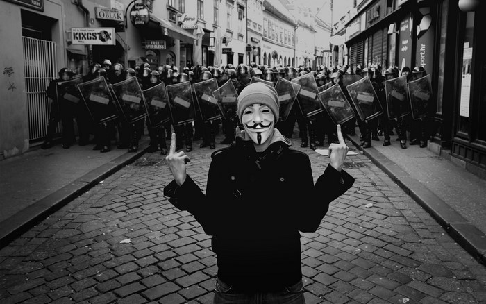 Guy in Guy Fawkes mask and riot police