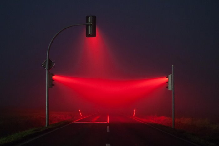 Red traffic lights illuminate a foggy road at night