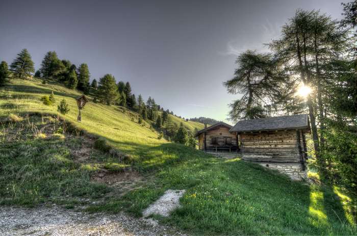 Wooden cabins on a grassy hillside with trees and a cross