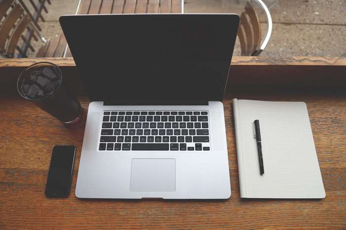 MacBook Pro, iPhone, notebook, and drink on a wooden table