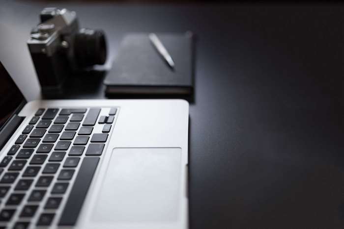 MacBook laptop, camera, notebook, and pen on a desk