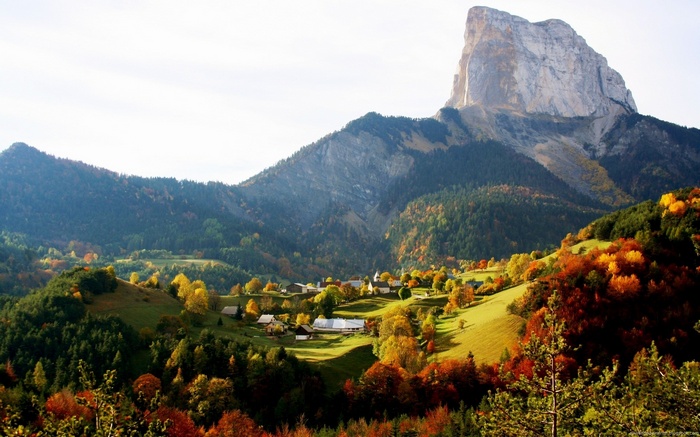 Mountain village in autumn with colorful trees and a large peak